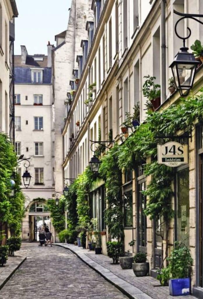 A charming cobbled street in the 11th arrondissement of Paris, lined with greenery-covered buildings, vintage lanterns, and local boutiques. A hidden gem in one of the city’s trendiest districts