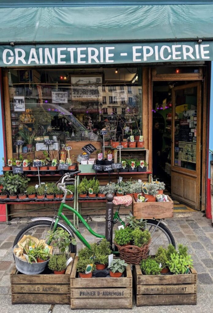 A traditional épicerie in the 12th arrondissement of Paris, featuring an outdoor display of potted plants, fresh herbs, and a vintage bicycle. A charming example of the district’s local commerce and community feel