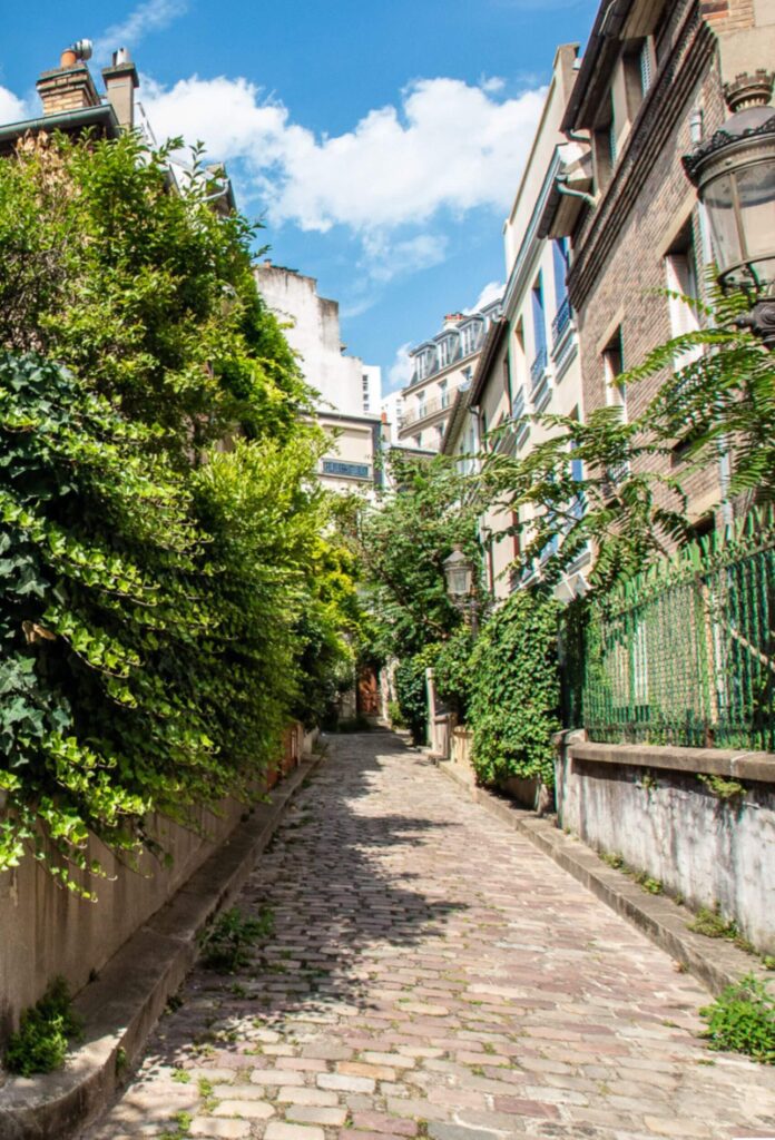 A charming cobbled street in the Butte-aux-Cailles neighborhood of the 13th arrondissement of Paris, lined with greenery-covered houses and historic buildings. A hidden gem with a village-like atmosphere in the heart of the city