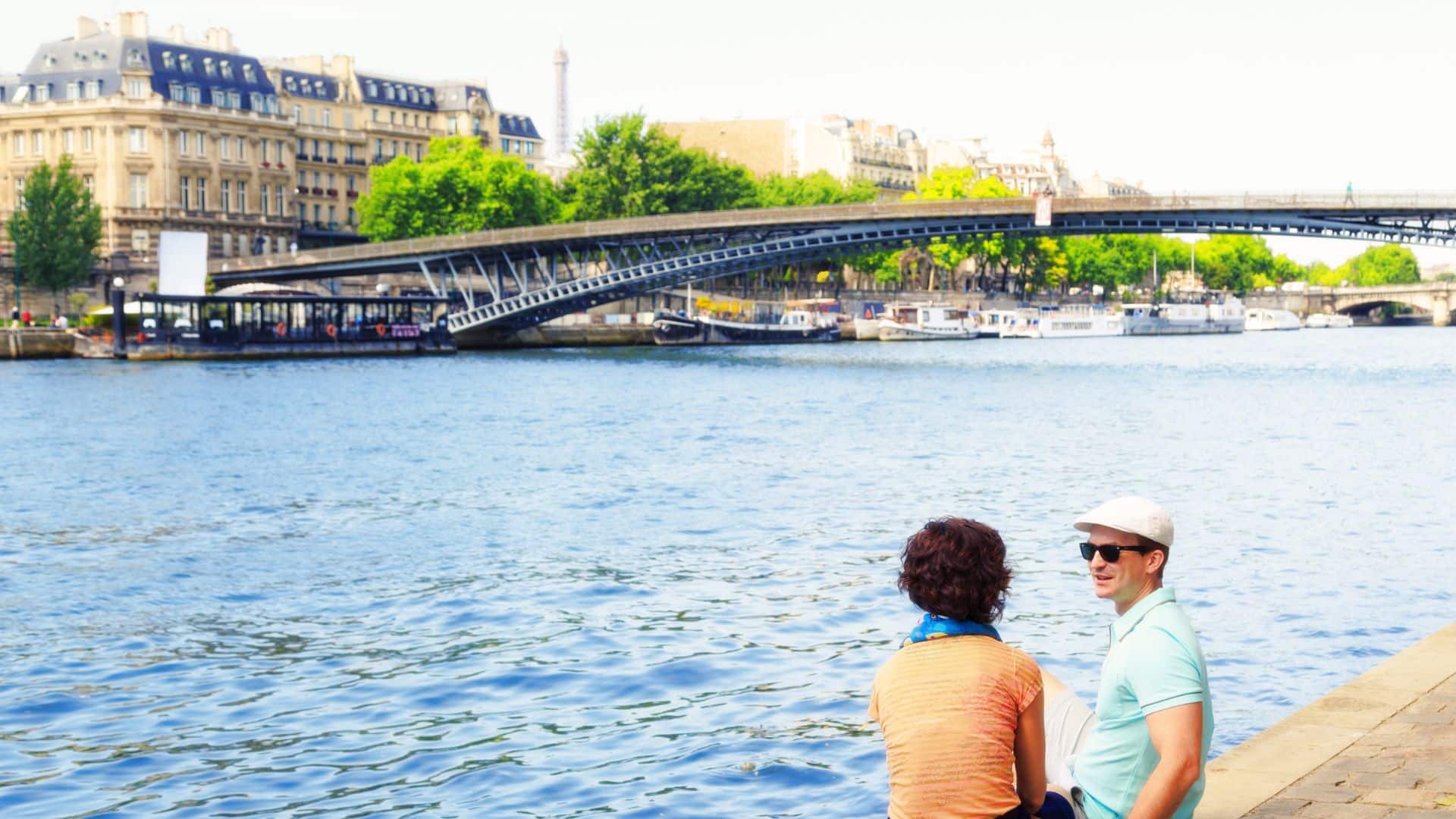 Couple relaxing on the Seine River banks in Paris 1st arrondissement with historic bridges and city view