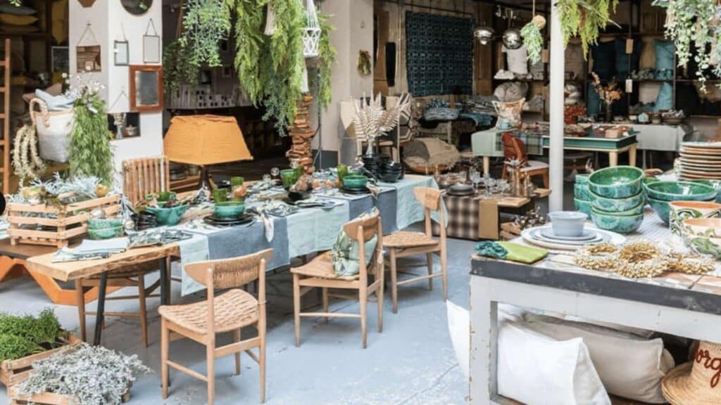 Rustic Parisian outdoor market stall with wooden chairs, tableware, and hanging plants.