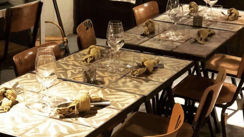 Restaurant tables with patterned cloth napkins and wine glasses set in intimate Parisian dining setting.
