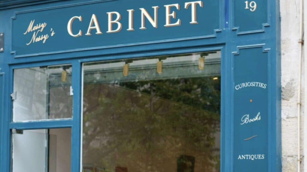 Blue Parisian shopfront with "CABINET" sign, offering curiosities, books, antiques.