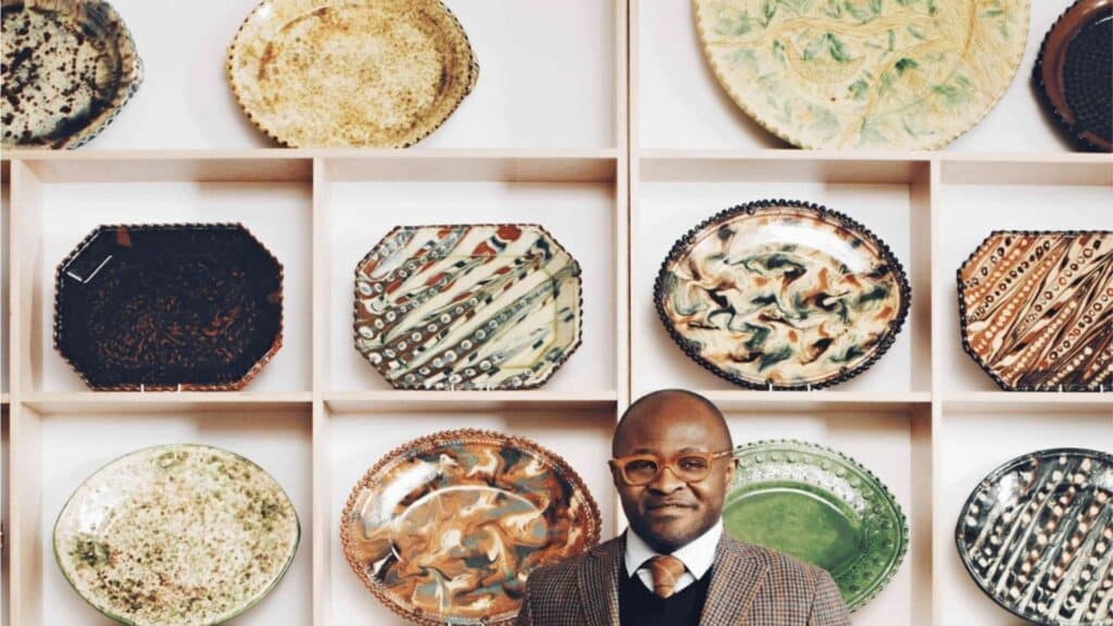 Man in front of decorative ceramic plates display on shelves.