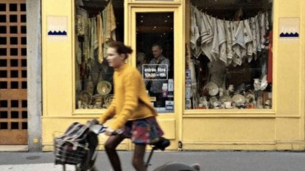 Person riding bicycle past a yellow storefront with textiles and pottery displayed in Paris.