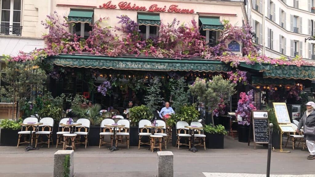 Parisian café "Au Chien Qui Fume" with floral facade and outdoor seating in Parisian architecture setting.