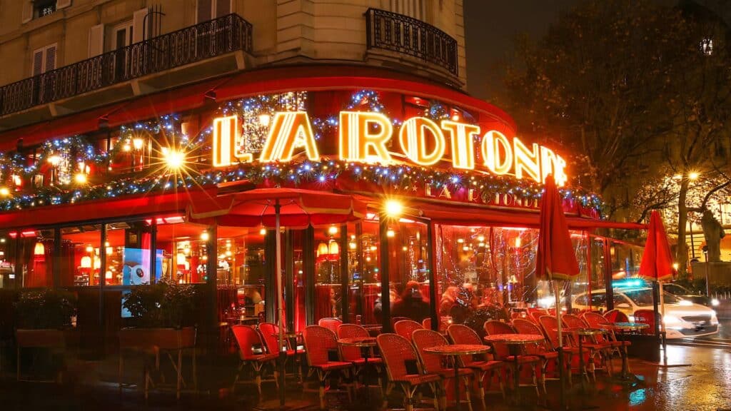 La Rotonde Montparnasse illuminated at night with outdoor seating, Paris.