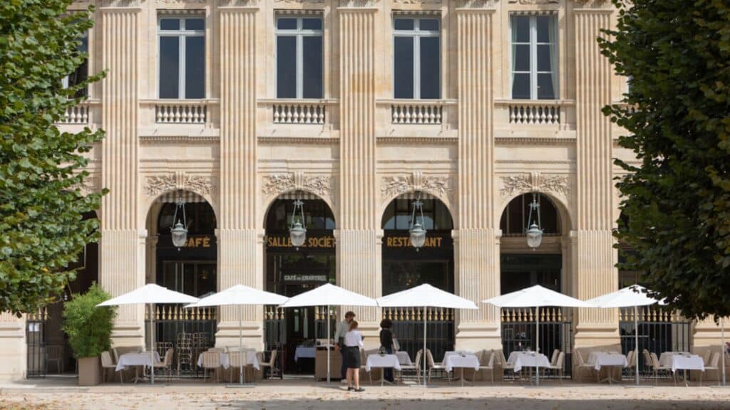 Historic Le Grand Véfour restaurant with classic Parisian façade and outdoor seating under white umbrellas.