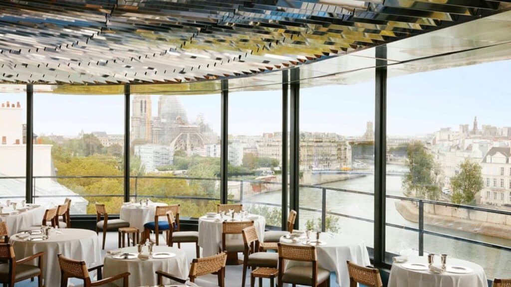 Elegant Parisian restaurant with Seine River view and Notre-Dame Cathedral in the background.
