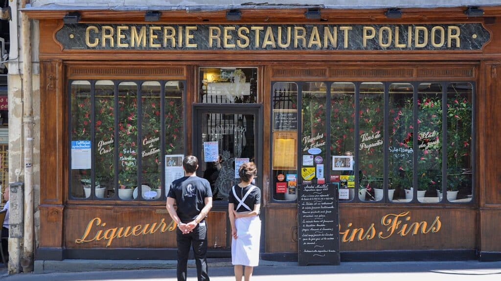 Historic Polidor restaurant facade in Paris with staff standing outside, featuring vintage signage and menu board.