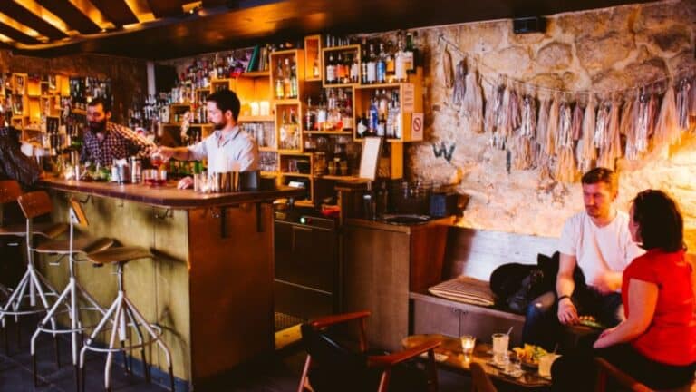 Cozy Parisian bar with stone walls, bartenders mixing drinks, and patrons seated at wooden tables.