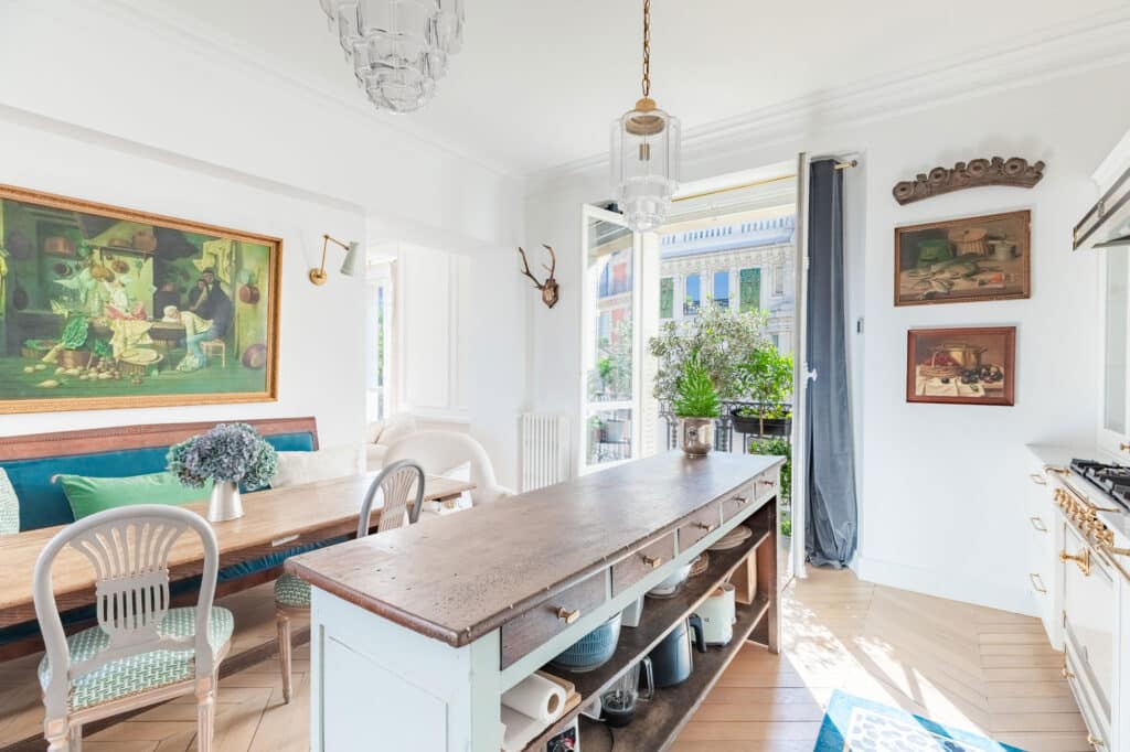 Renovated Parisian kitchen with parquet floor, vintage dining area, and large window with city view.