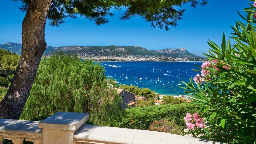 Scenic coastal view with blue sea, sailboats, and green hillside, perfect for day trips from Paris.